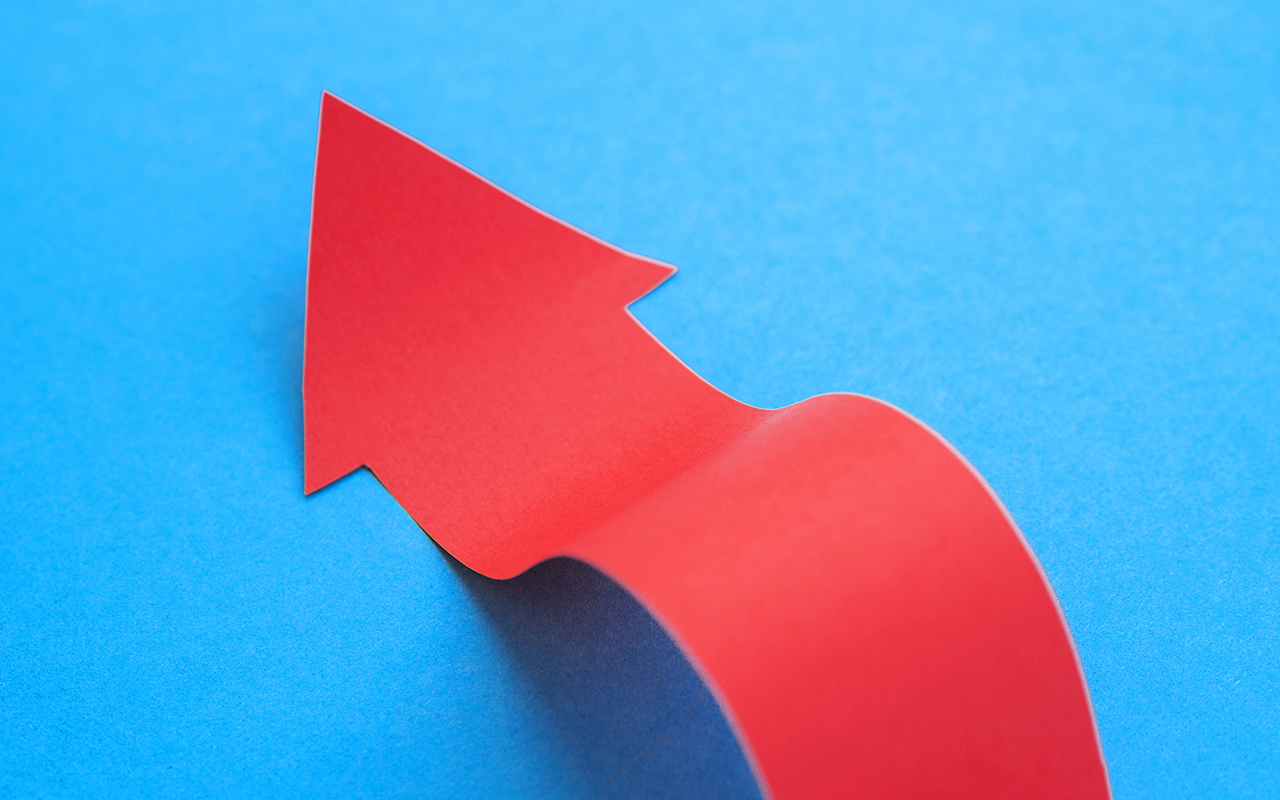 A red paper arrow directed upward against a vibrant blue background, symbolizing progress and direction