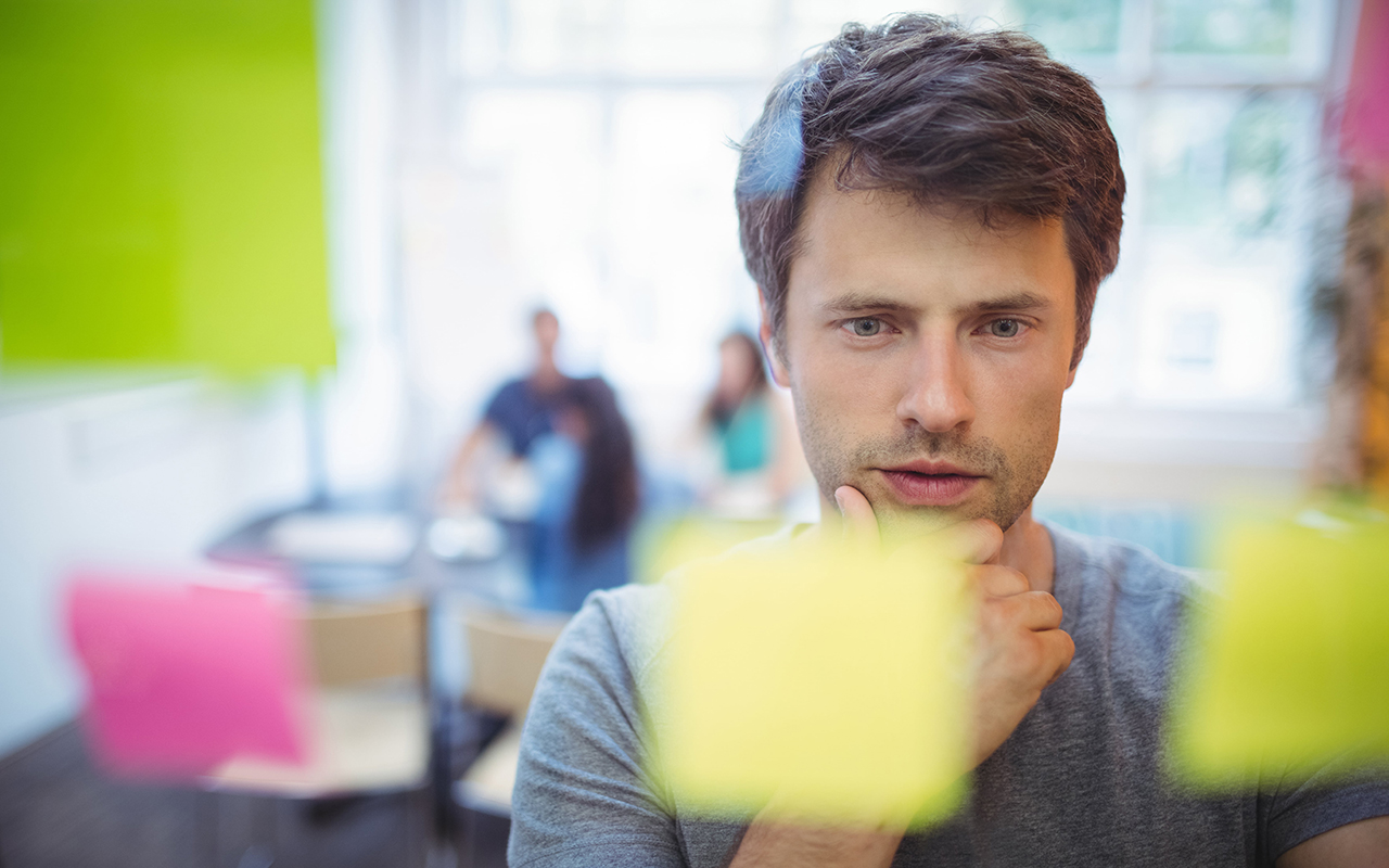 A man stands in front of a wall covered in colorful sticky notes, deep in thought and contemplation